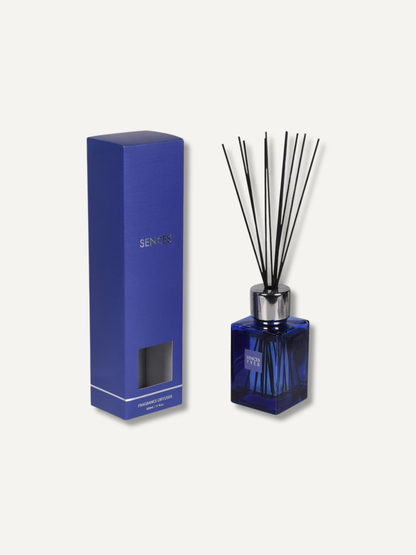 A reed diffuser set featuring a dark blue glass bottle with black reeds and a matching dark blue rectangular box, shown on a light off-white background.
