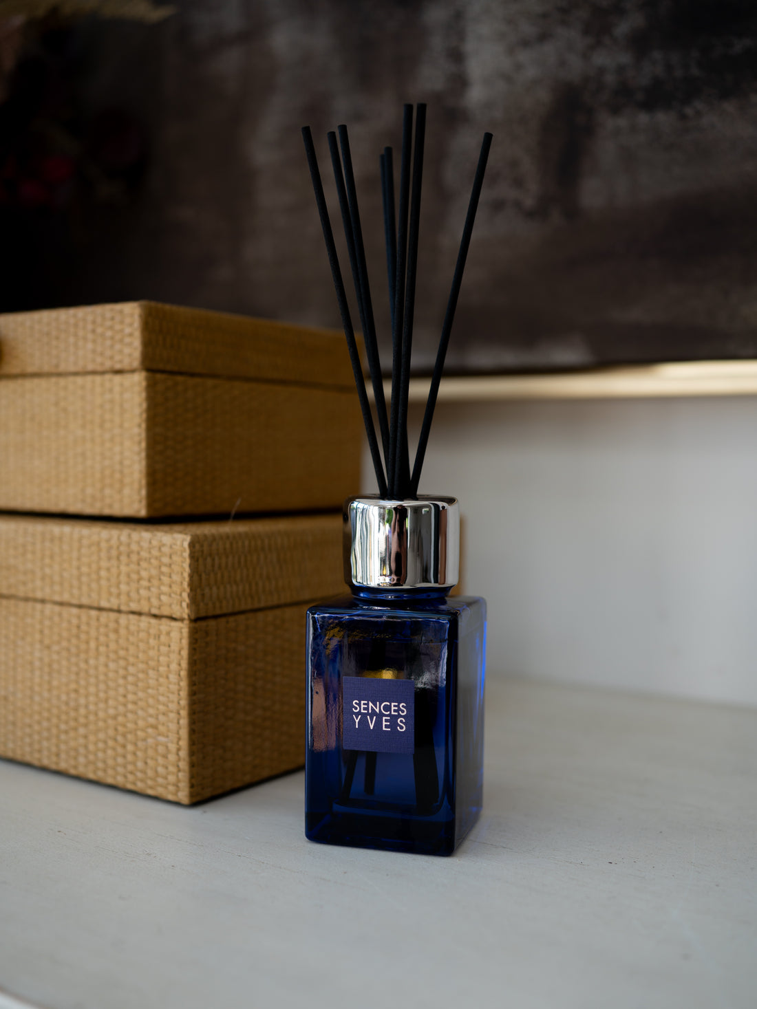 A blue glass reed diffuser bottle with black reeds and a silver cap, labeled &