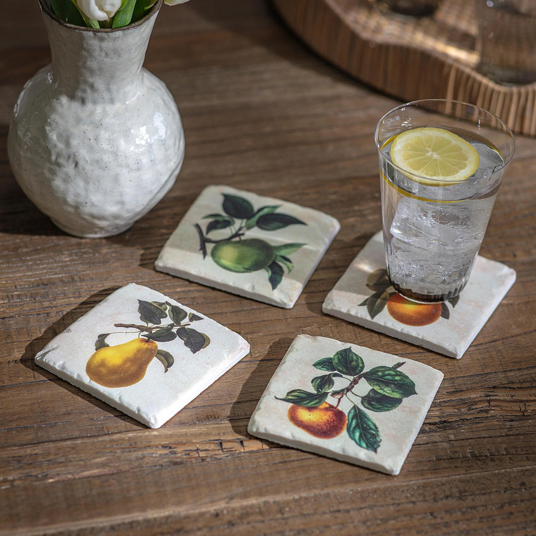 Coasters with apple and pear designs on a wooden surface with a glass of water and lemon.