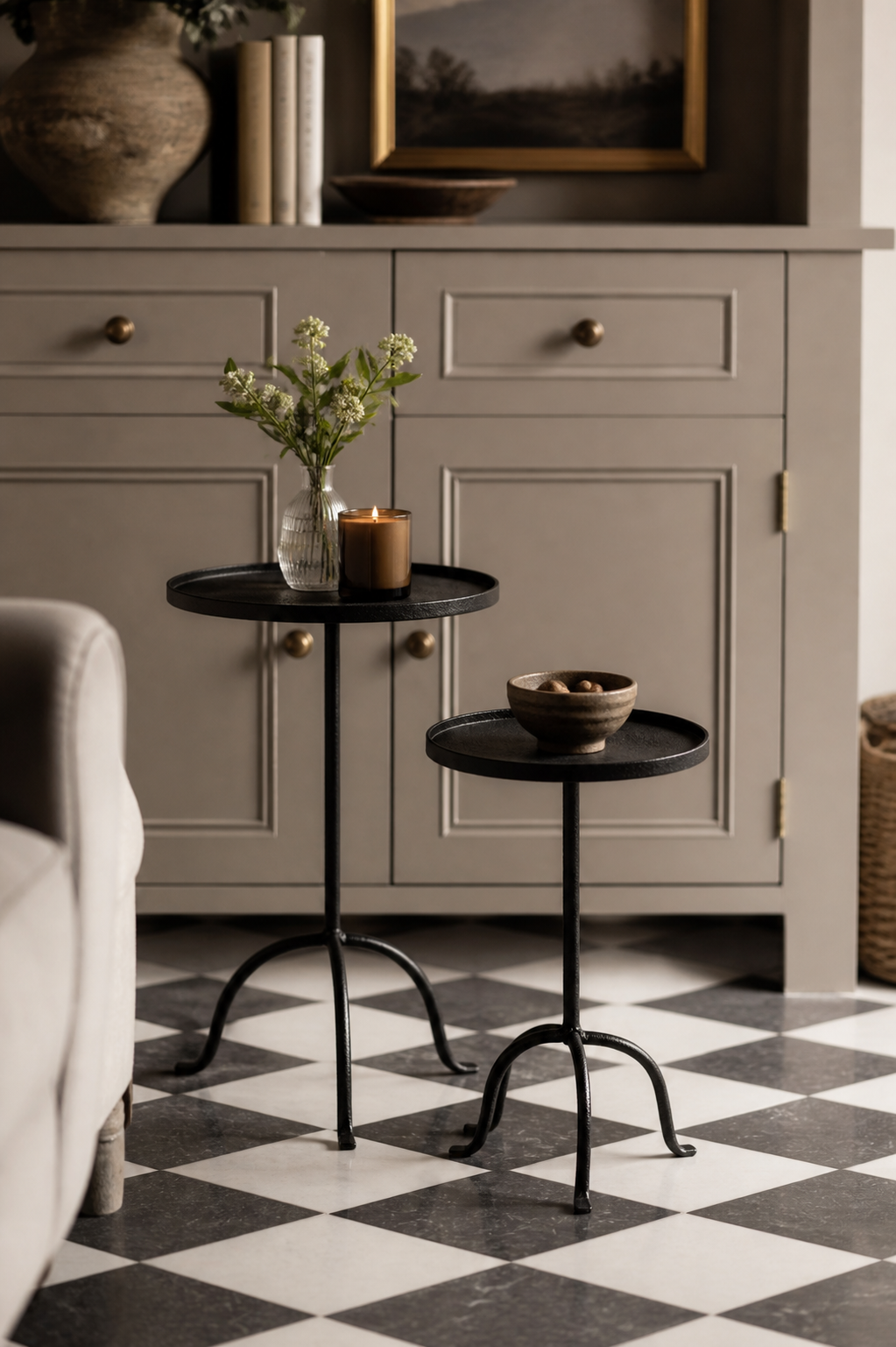 Two black metal side tables with decorative items in a room with gray cabinets and a checkered floor.