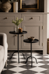 Two black metal side tables with decorative items in a room with gray cabinets and a checkered floor.