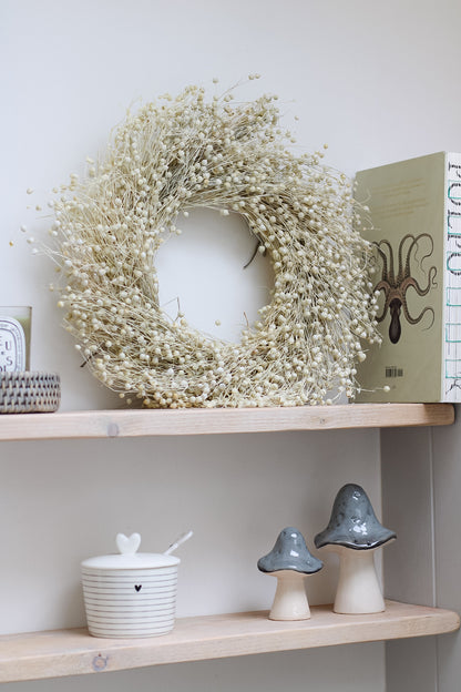 A bleached dried linum wreath displayed on a shelf with other home decor items.