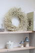 A bleached dried linum wreath displayed on a shelf with other home decor items.