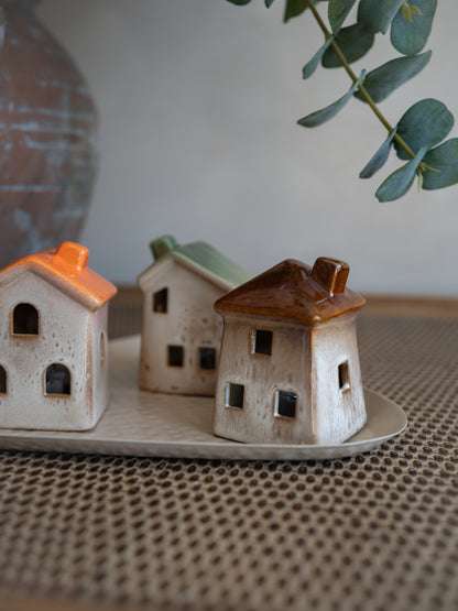 Three small ceramic house-shaped  with LED lights in different coloured roofs, displayed on a matching tray on a woven placemat.