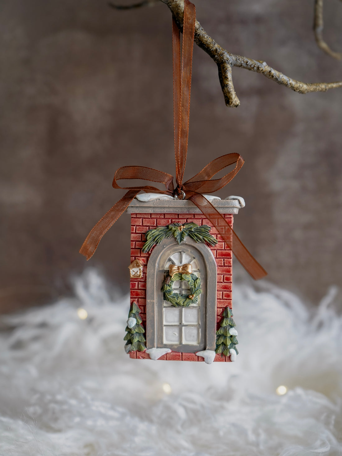 Decorative Christmas ornament resembling a brick building with a wreath, hanging on a branch.