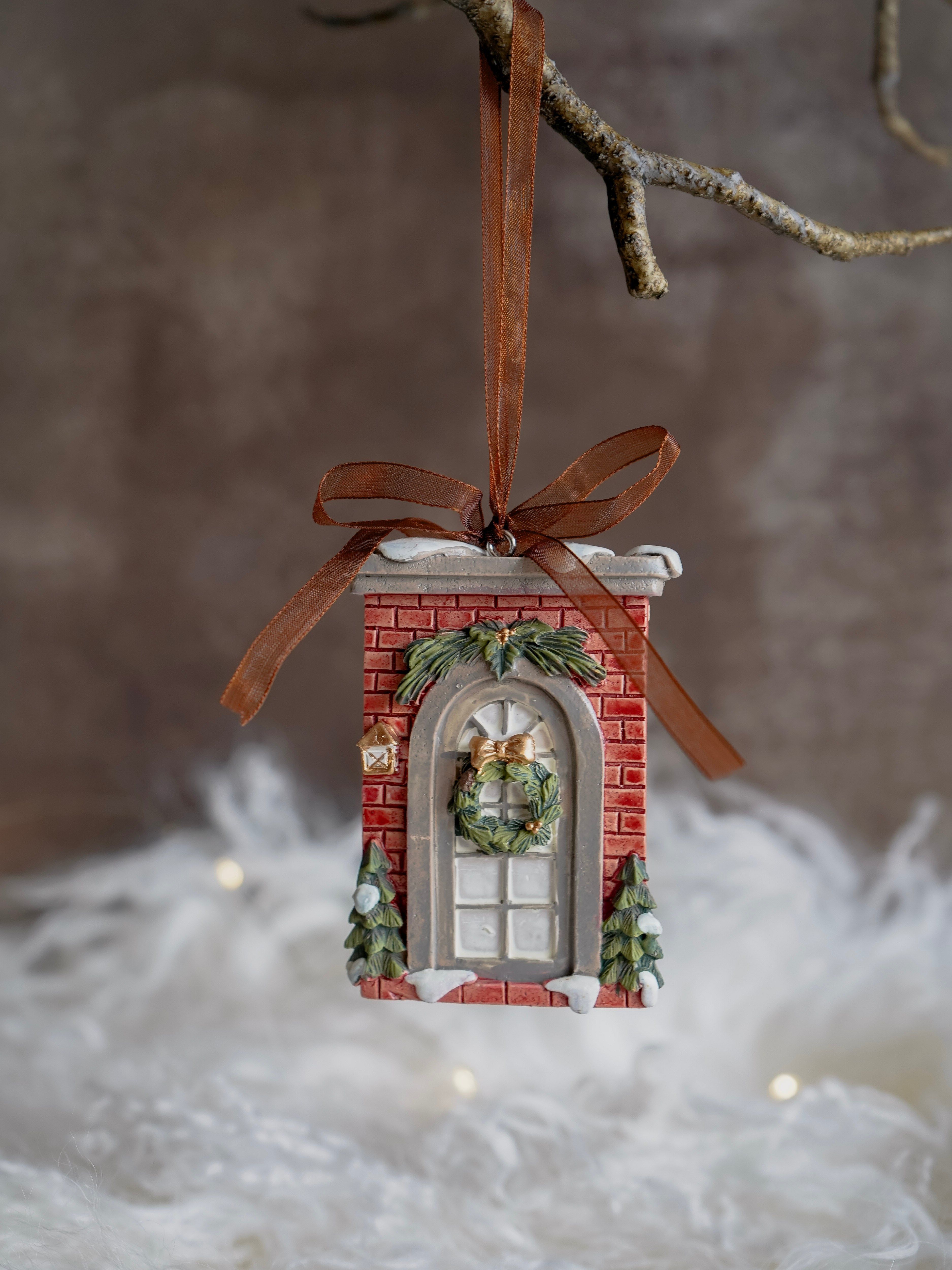Decorative Christmas ornament resembling a brick building with a wreath, hanging on a branch.