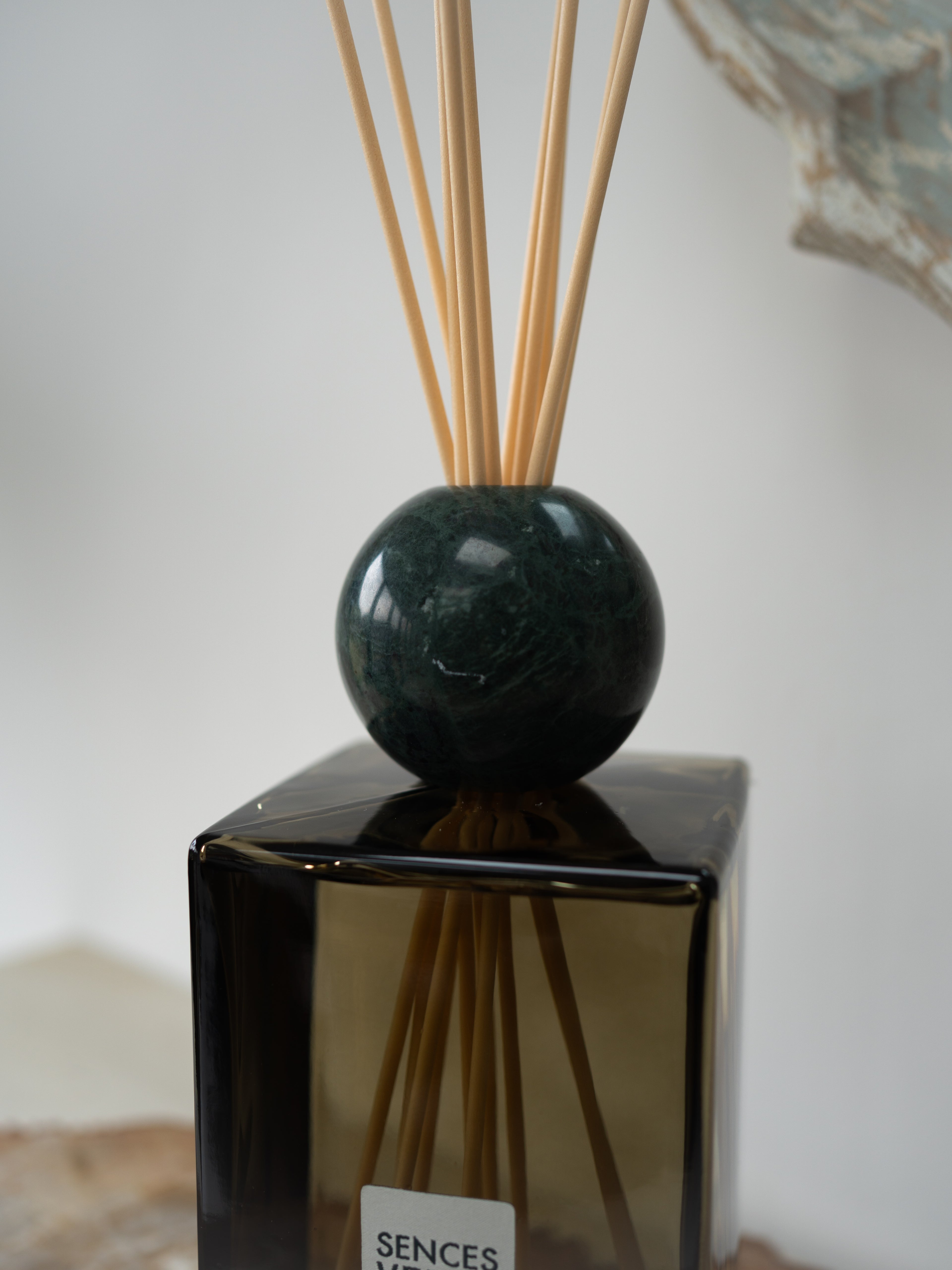 A reed diffuser with a dark green marble sphere and natural wood reeds, set in a square dark green glass bottle with a visible SENCES label.