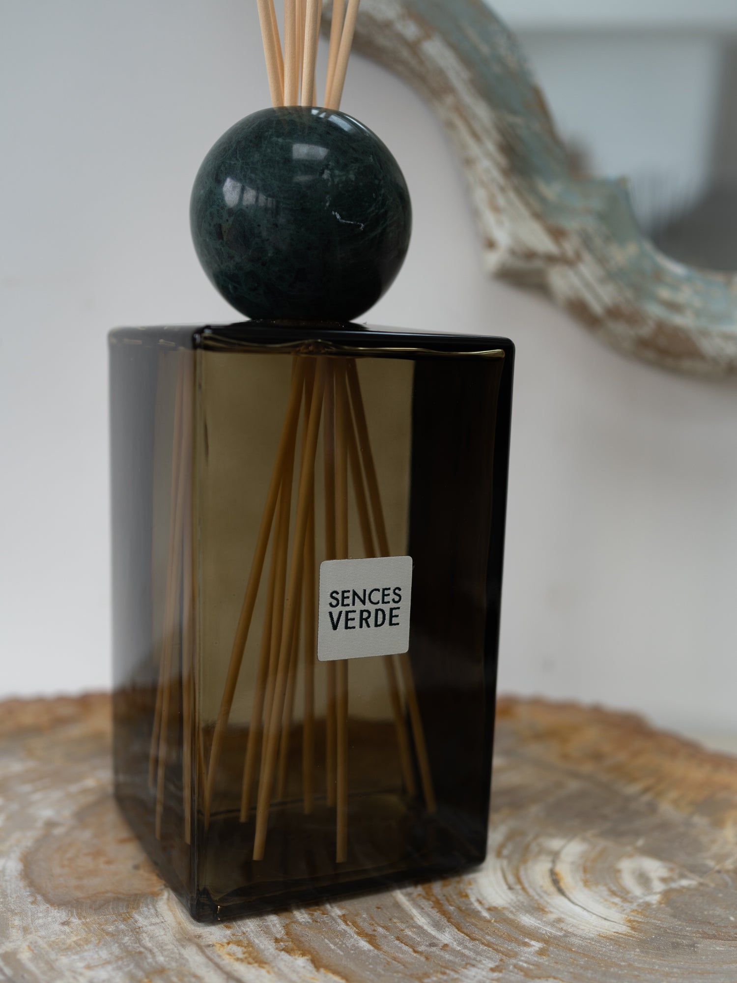 A Sences Verde reed diffuser with a dark green glass bottle, a polished dark green marble sphere, and natural reed sticks, resting on a rustic wood slice.