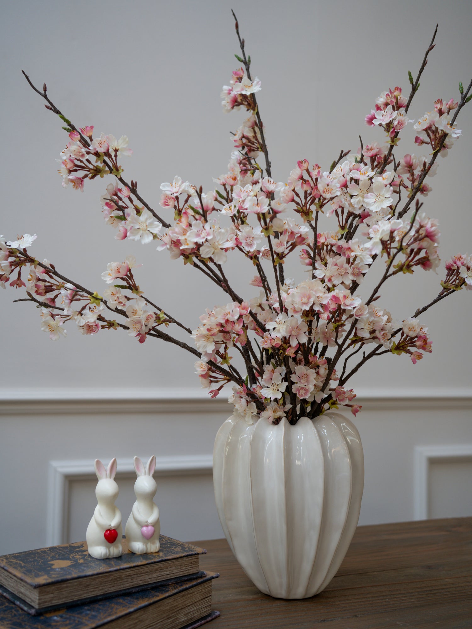 Vase with cherry blossom branches on a table with books and rabbit figurines.