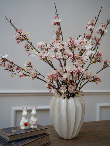 Vase with cherry blossom branches on a table with books and rabbit figurines.