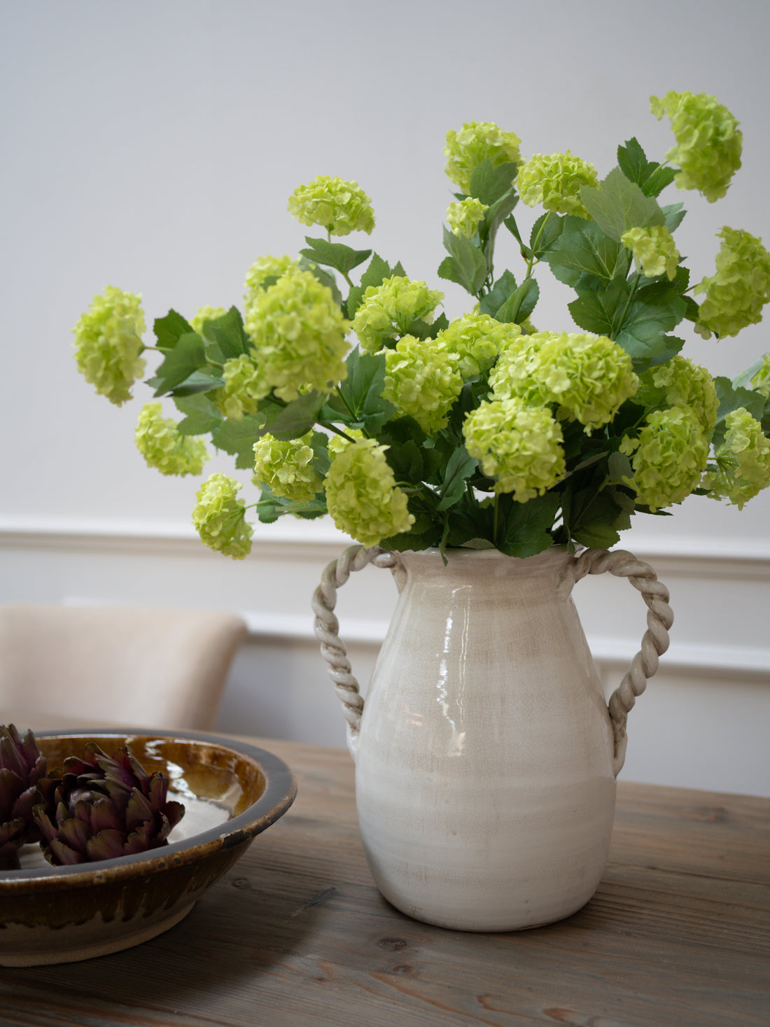White rustic vase with twisted handles vase with green snowball flowers on a wooden table