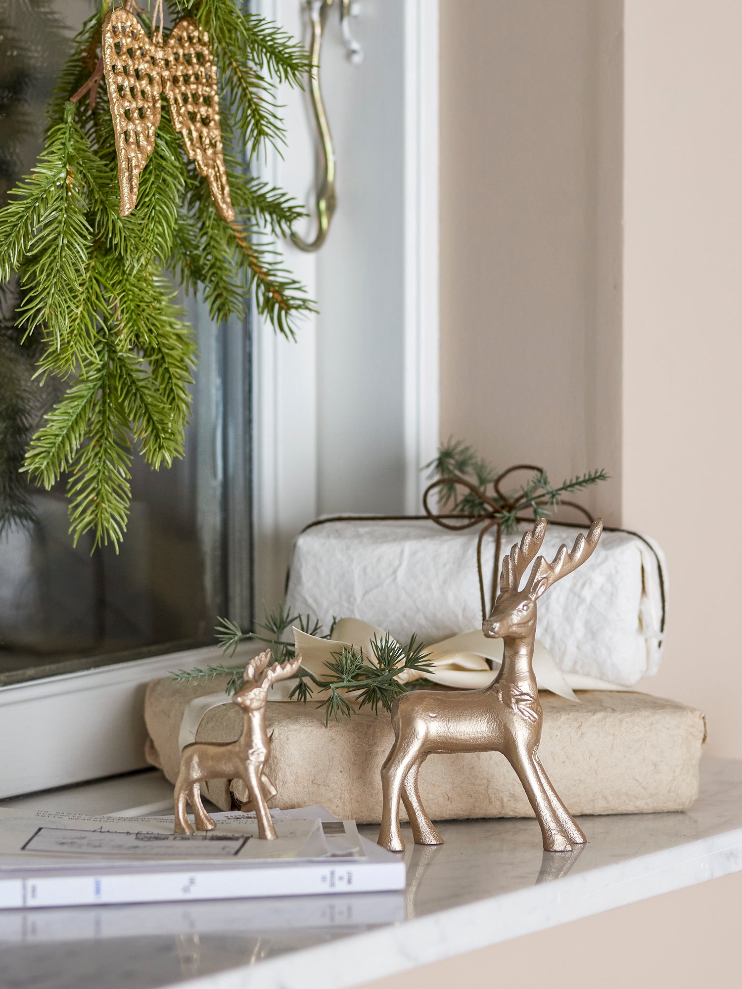 Decorative scene with gold christmas reindeer figurines, greenery, and wrapped gifts on a surface.