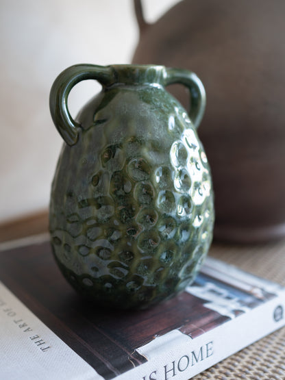 Green textured ceramic vase on a surface with a blurred background