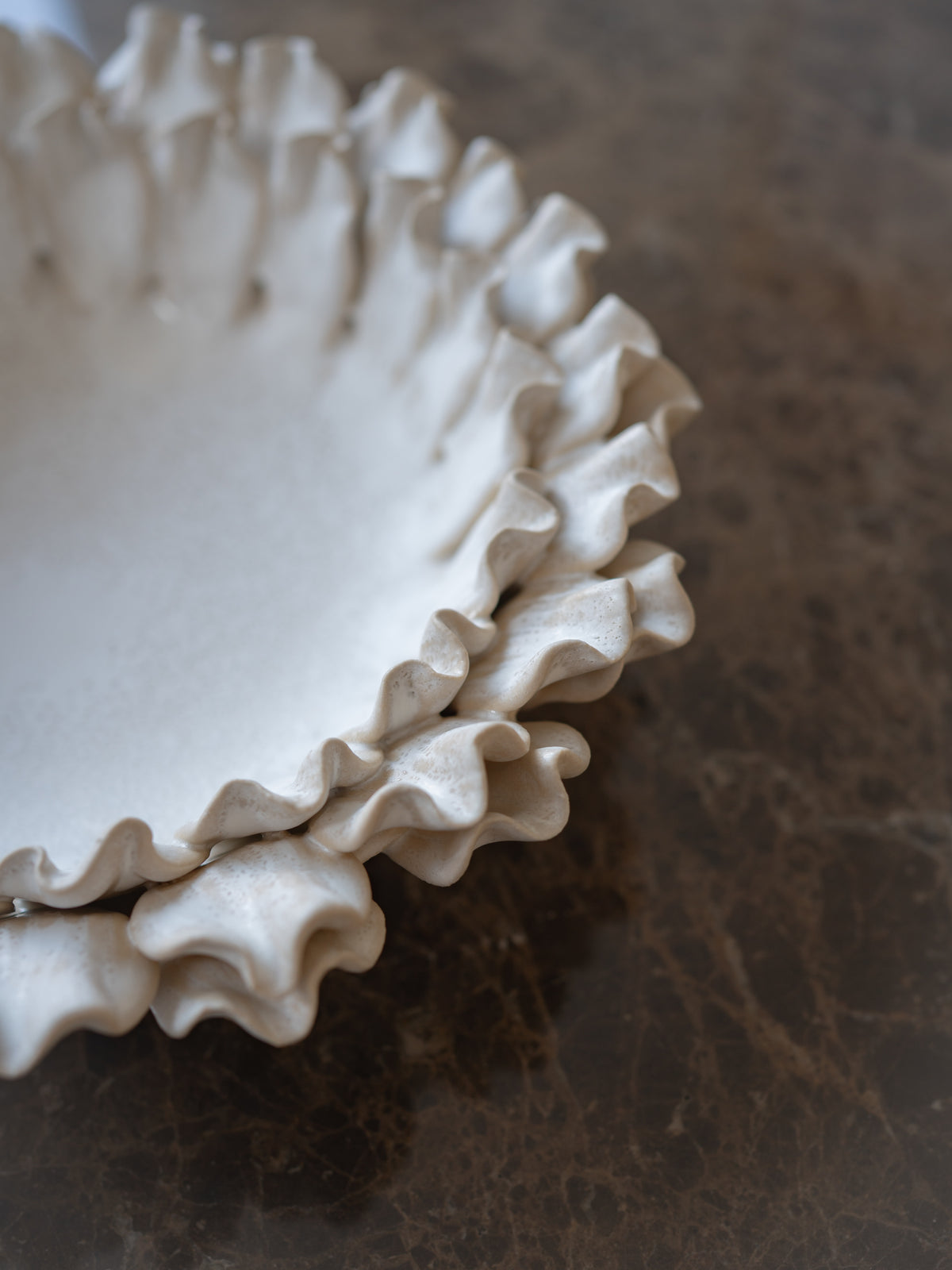 A close-up of a white ceramic bowl with a ruffled edge, resting on a dark brown marble surface.