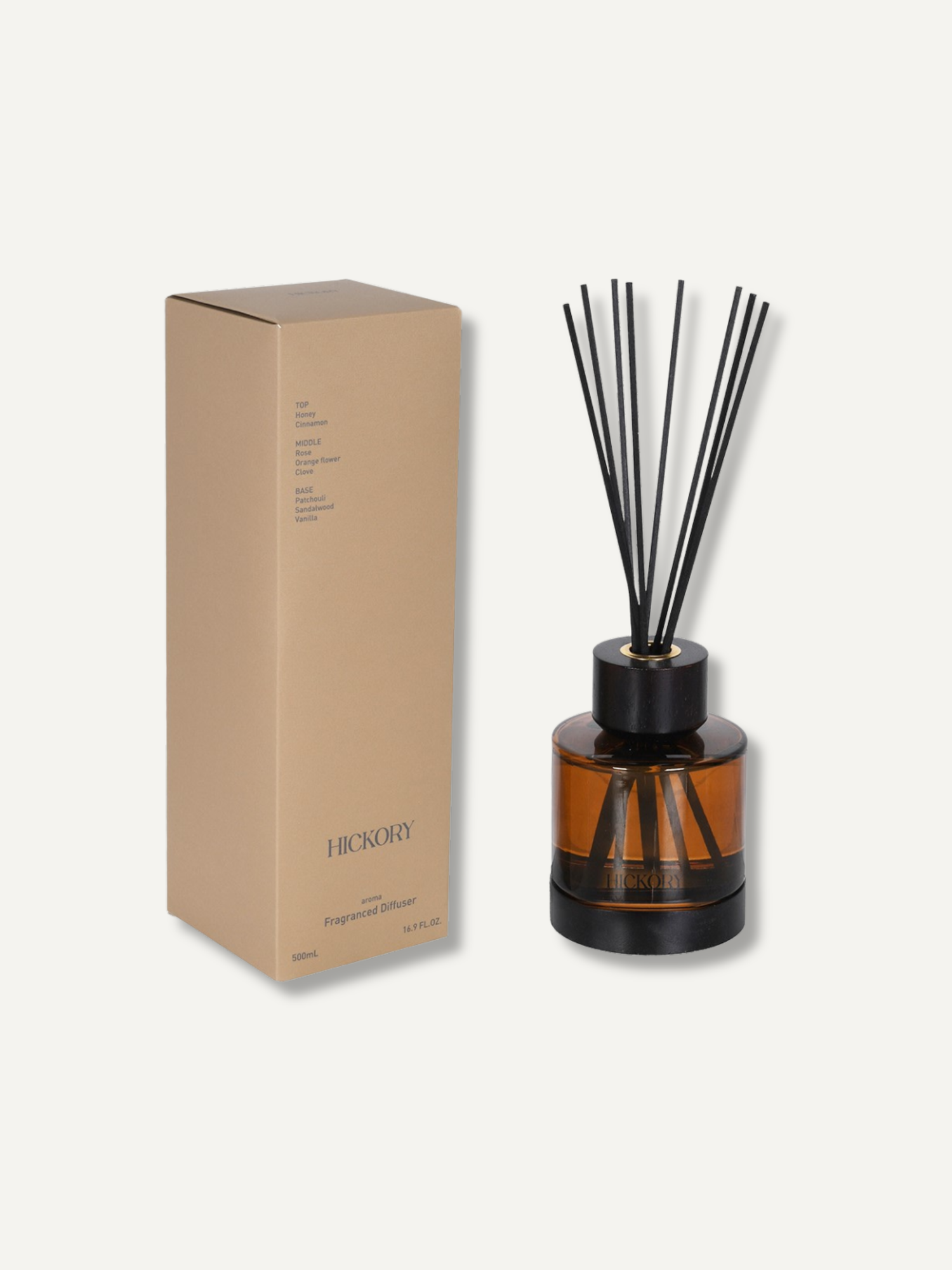 An amber glass reed diffuser bottle with black reeds and a black cap, shown next to its tan cardboard packaging box on a light off-white background. The box is labeled &