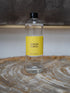 A clear plastic bottle of SENCES NEROLI reed diffuser refill oil with a bright yellow label and black cap, resting on a rustic wood slice coaster.