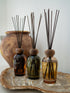 Three balearic inspired diffuser bottles with reeds on a wooden tray against a white background