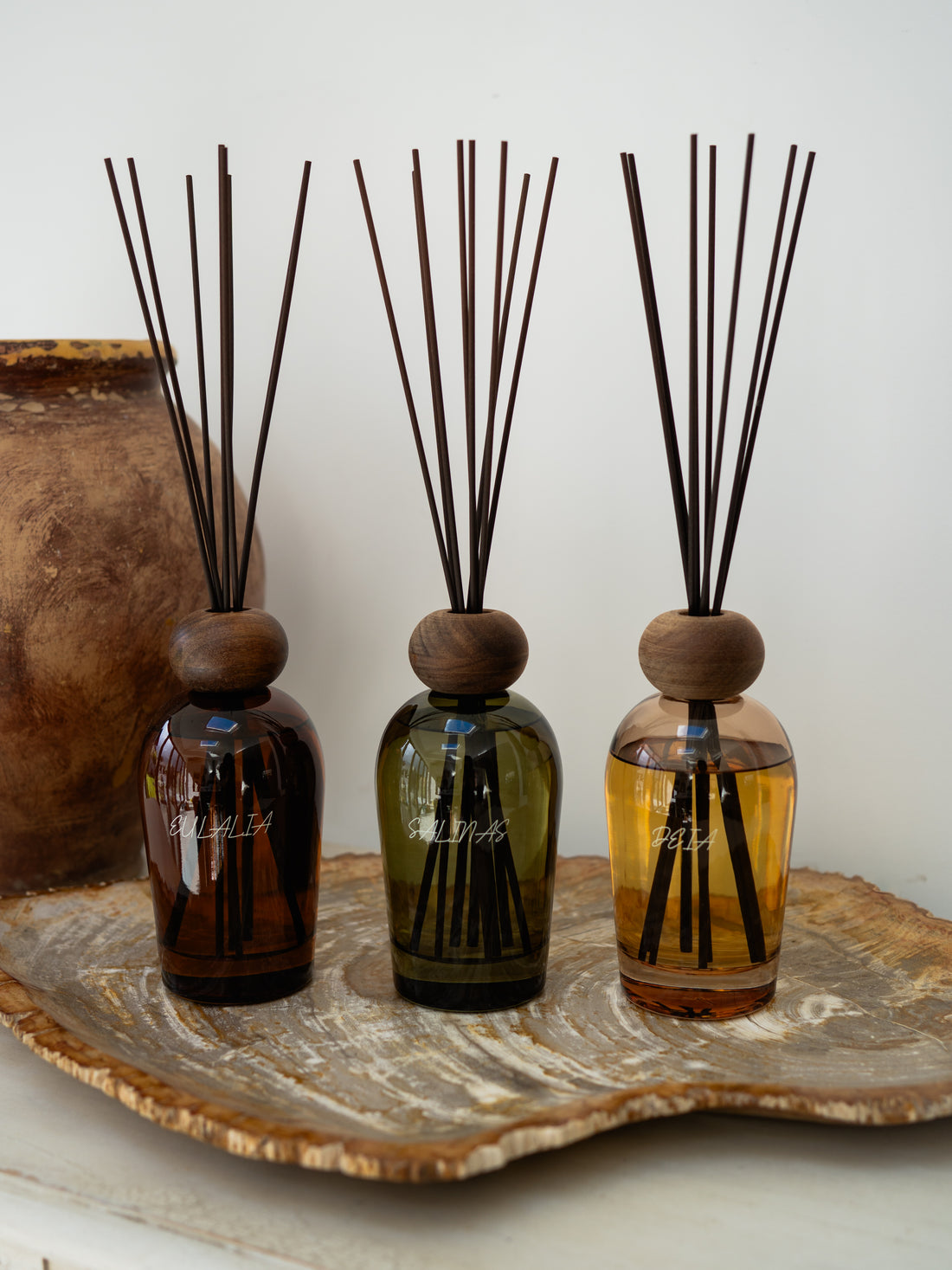 Three diffuser bottles with wooden caps and reeds on a decorative stone surface.