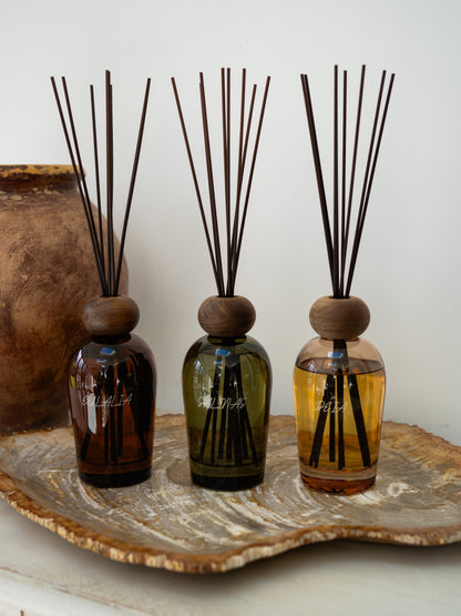 Three diffuser bottles with wooden caps and reeds on a decorative stone surface.