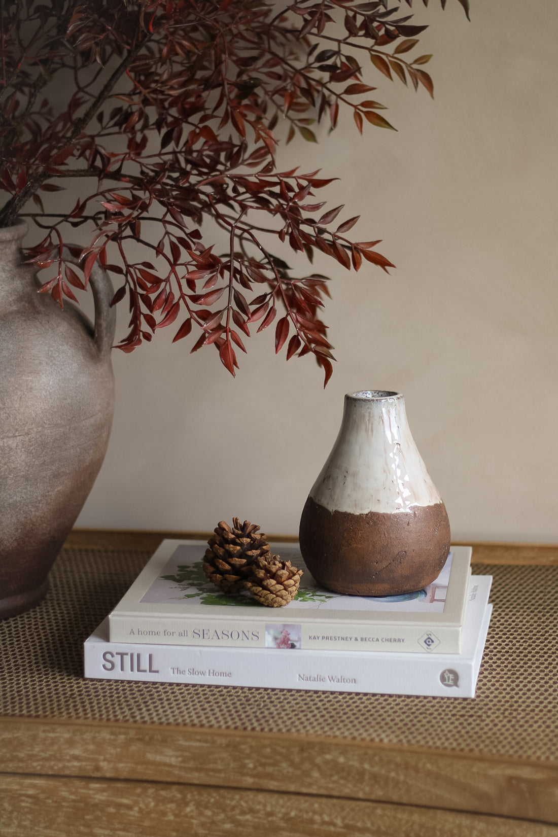 Decorative setting with a vase, books, and branches on a wooden surface.