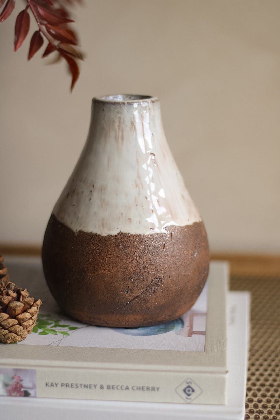 Ceramic vase with two-tone finish on a surface with books and a pine cone.