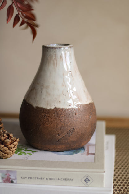 Ceramic vase with two-tone finish on a surface with books and a pine cone.