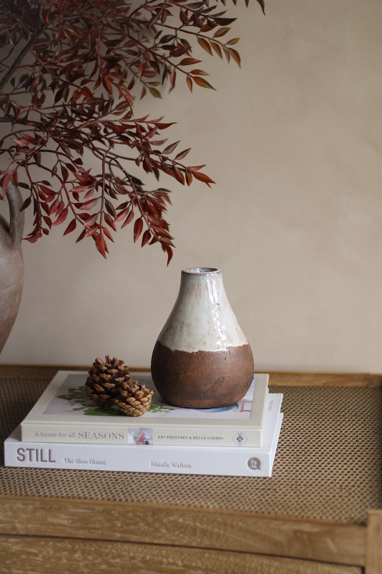 Ceramic vase on books with a branch and pine cone on a wooden surface