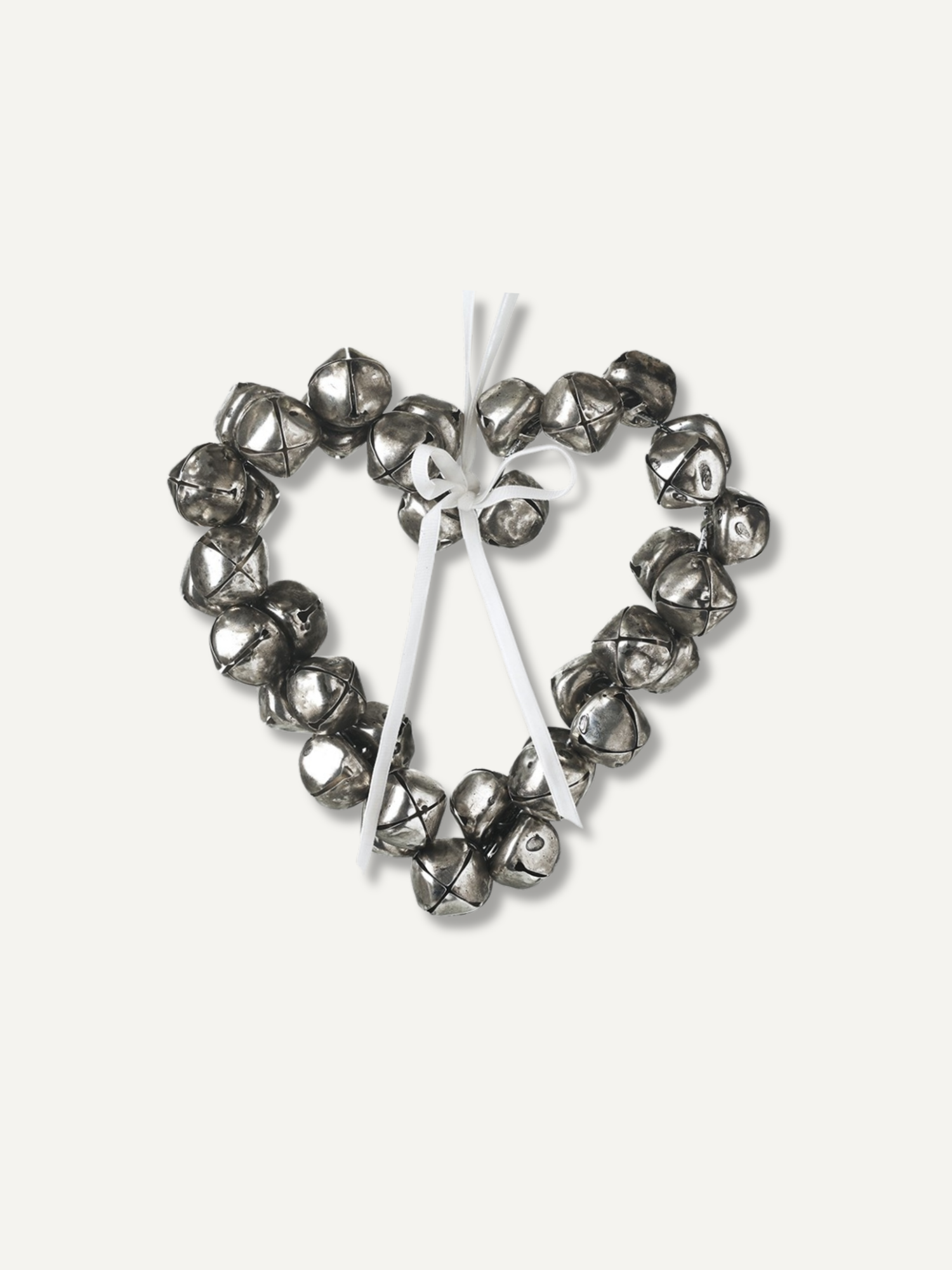 A heart-shaped metal wreath decoration made of small silver bells tied together with a white ribbon, shown on a plain off-white background.