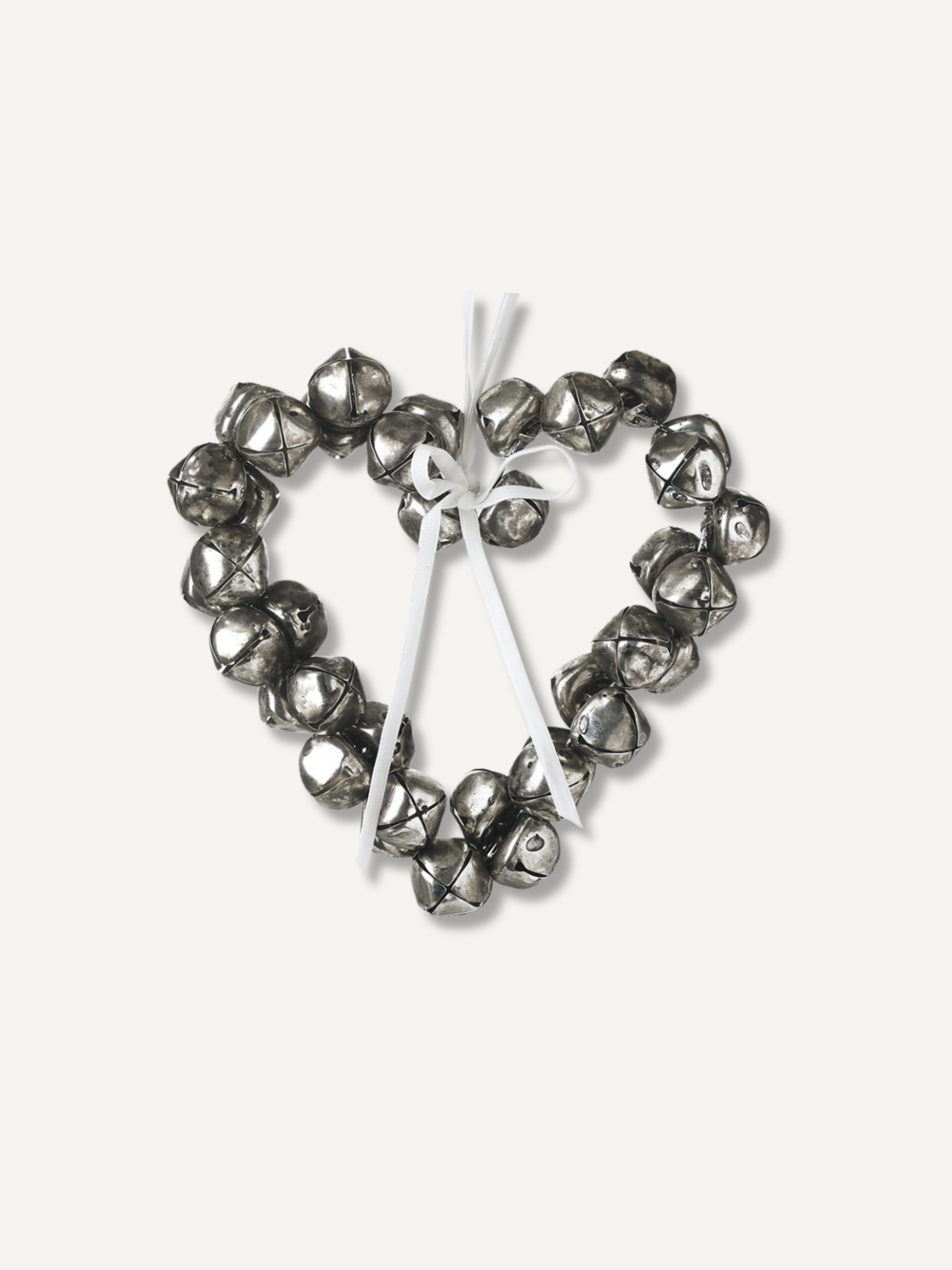A heart-shaped metal wreath decoration made of small silver bells tied together with a white ribbon, shown on a plain off-white background.