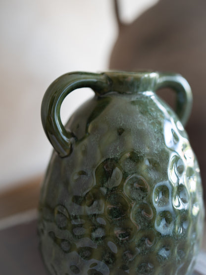 Green ceramic vase with textured surface and handles on a blurred background