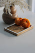 A small mango wood tray with white edge detailing, placed on a table with a vase of flowers and two orange pumpkins on top.