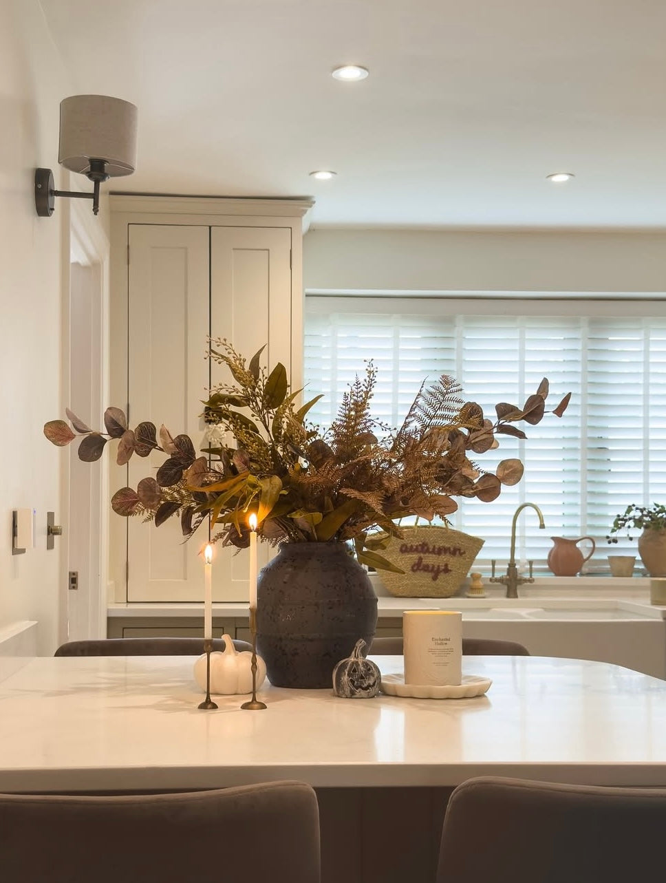 Dining area with a vase of flowers on a table, candles, and a window in the background.