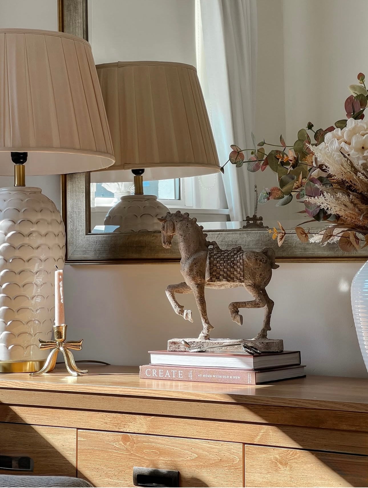 Decorative horse statue on books with lamps and a mirror in the background