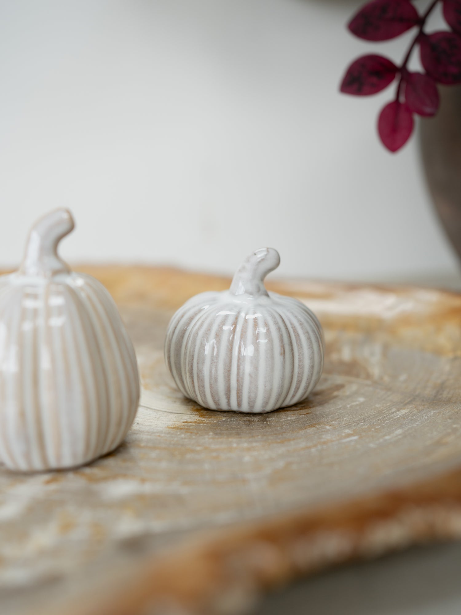Two small ribbed ceramic pumpkins in off-white and light gray, styled on a wooden serving board with a blurred neutral background.