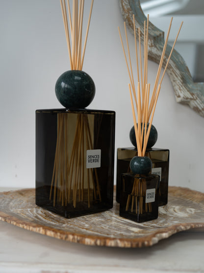 three green glass reed diffusers with dark green marble spheres and natural reed sticks, displayed on a decorative tray against a soft neutral background.