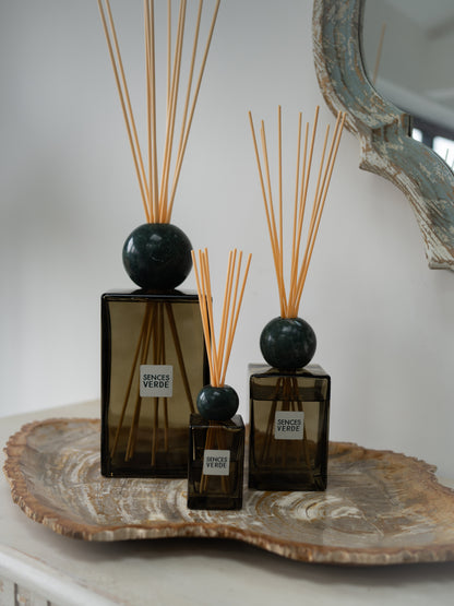 Three Sences Verde reed diffusers in amber glass bottles with dark green spherical marble tops and natural reed sticks, arranged on a decorative tray against a soft neutral background.