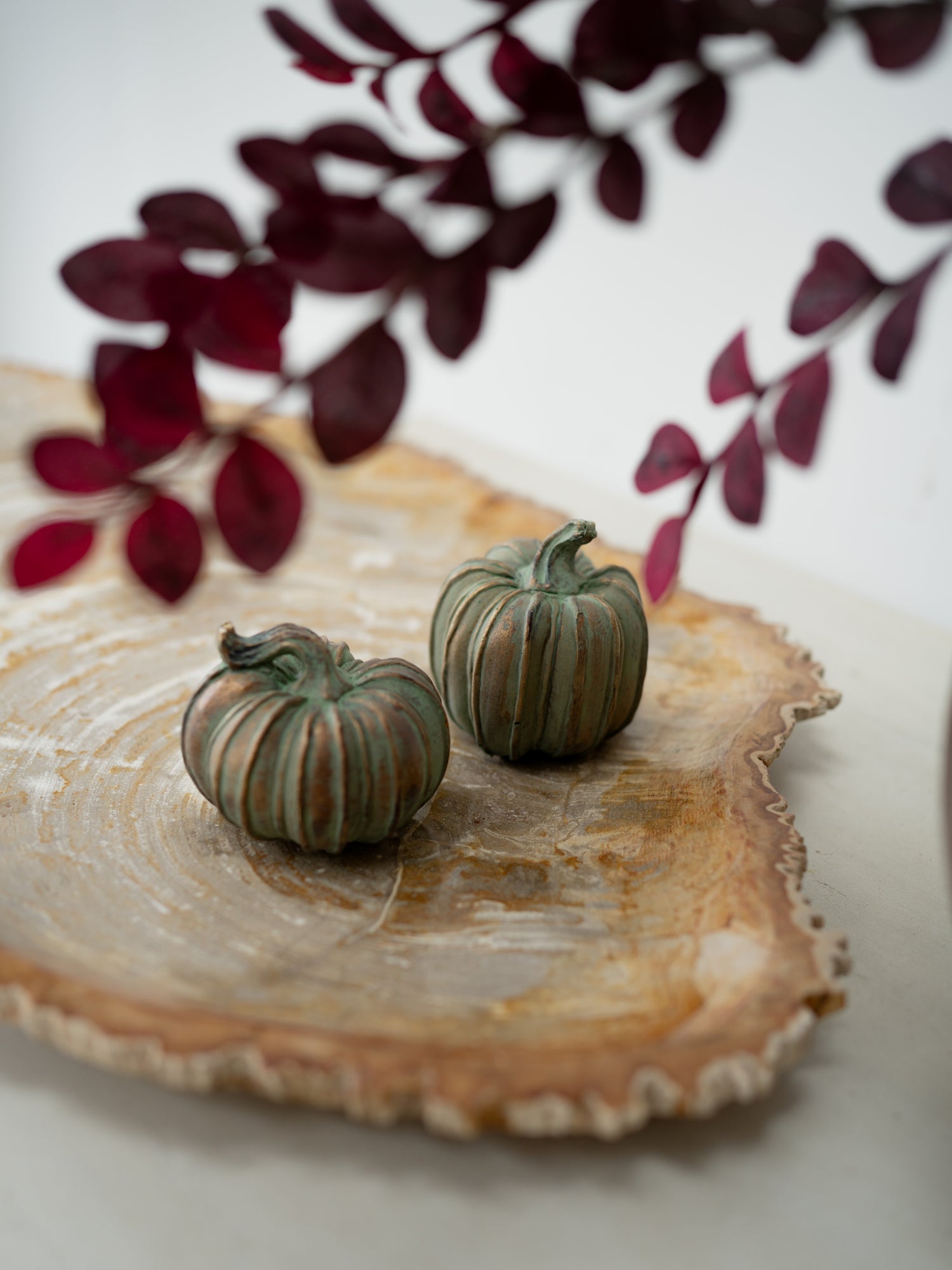 pair of verdigris pumpkins on fossilised board with faux plums in the foreground, autumn inspired home styling
