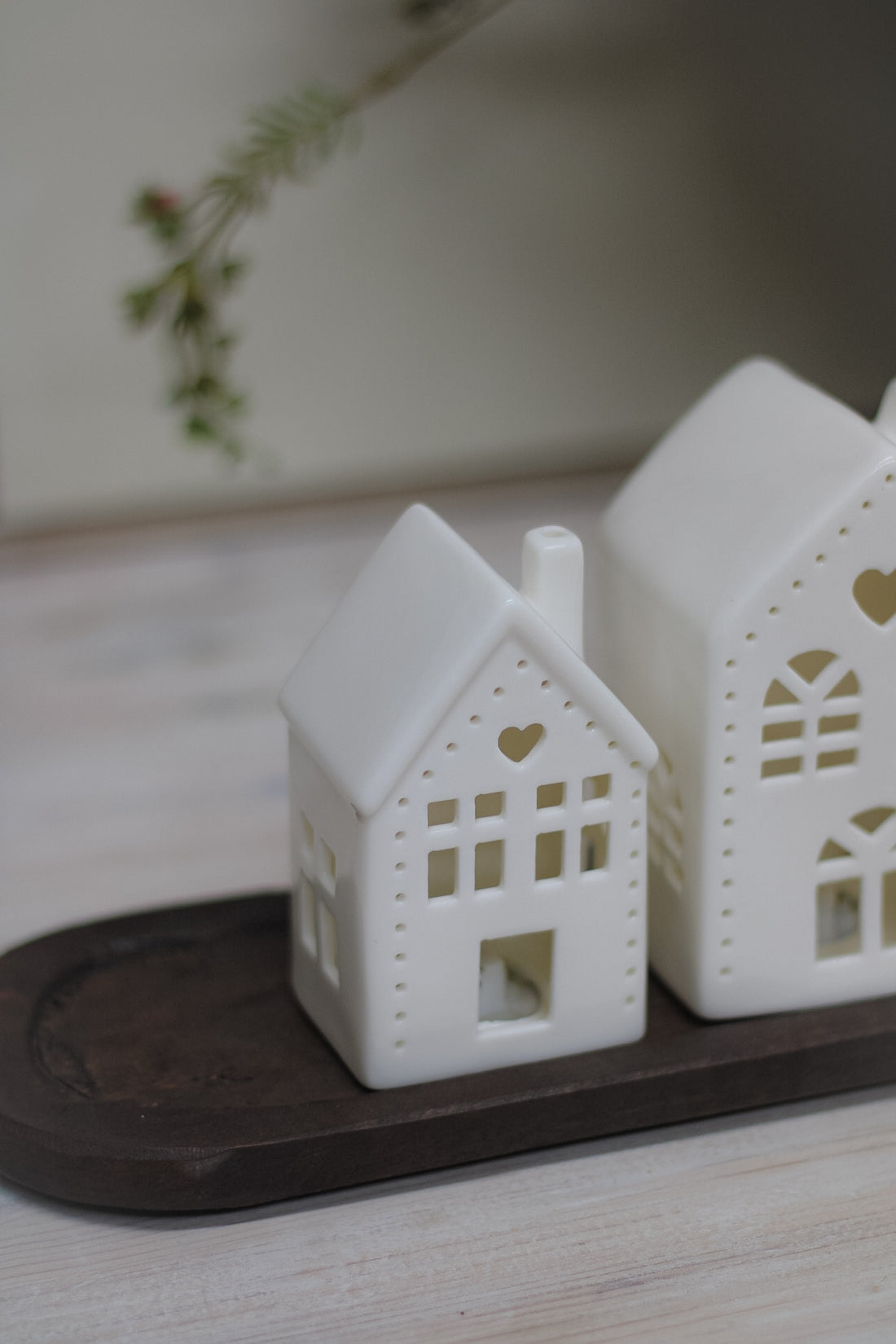 White ceramic houses with cut-out hearts and dots design, illuminated from the inside by LED lights, placed on a wooden surface.