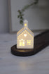 White ceramic houses with cut-out hearts and dots design, illuminated from the inside by LED lights, placed on a wooden surface.