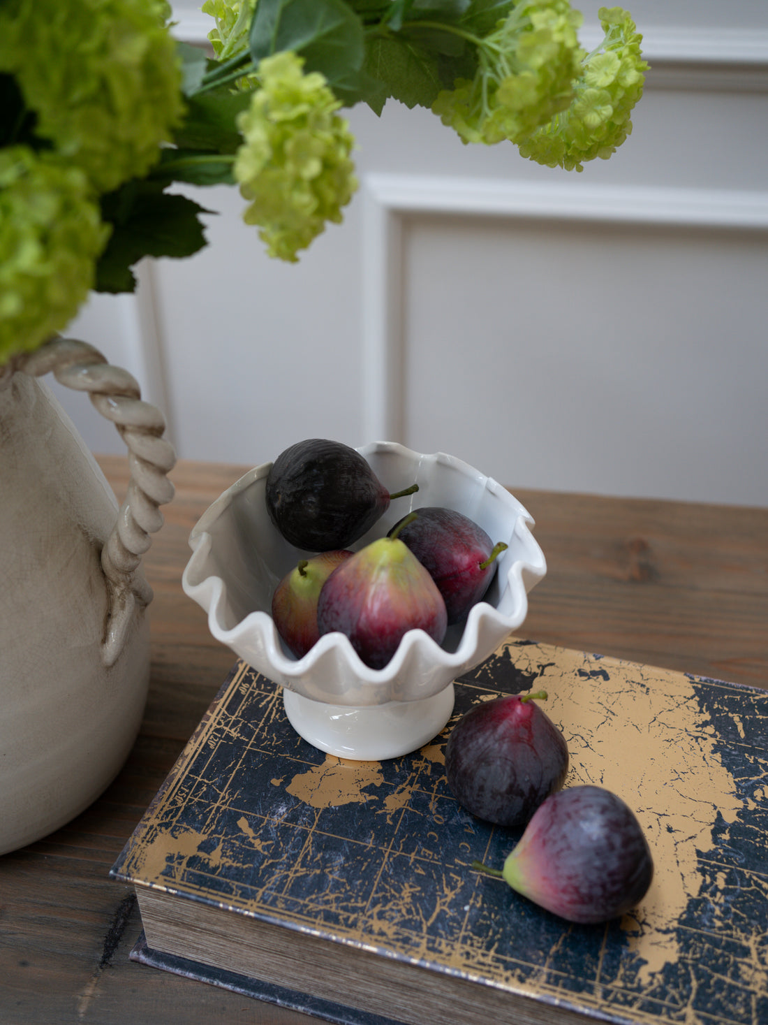 White scalloped-edge bowl with figs on a textured surface next to a vase of green flowers. Beautiful home decor and styling ideas for a timeless styled home.