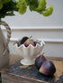White decorative bowl with faux figs on a textured surface with a floral arrangement in the background. Beautiful home decor and styling