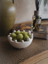 Small white bowl with green decorative echinops balls on a textured surface